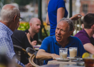 Older man sitting outdoors at a cafe table with a cup of coffee
